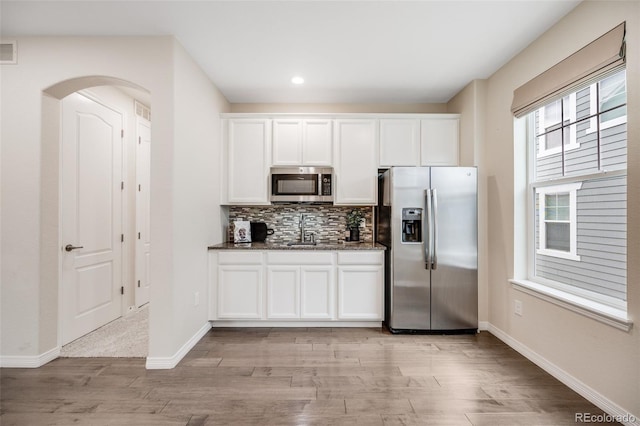 10387 Harrisburg St, Parker, CO 80134 - kitchen with appliances with stainless steel finishes, arched walkways, decorative backsplash, light wood finished floors, and white cabinets