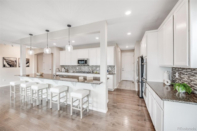 10387 Harrisburg St, Parker, CO 80134 - kitchen featuring stainless steel appliances, light wood-type flooring, tasteful backsplash, white cabinets, and a kitchen bar