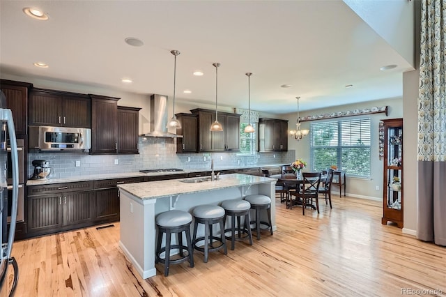23503 E Minnow Dr, Aurora, CO 80016 - kitchen featuring wall chimney range hood, appliances with stainless steel finishes, backsplash, light wood finished floors, and dark brown cabinets