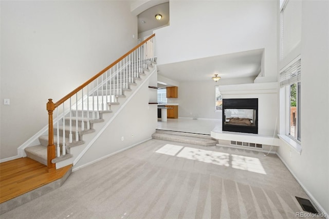 1272 Braewood Ave, Highlands Ranch, CO 80129 - unfurnished living room featuring a towering ceiling, stairs, baseboards, a multi sided fireplace, and carpet floors