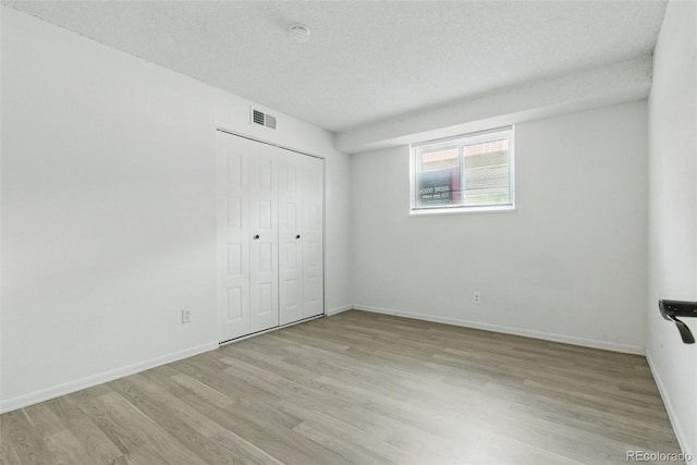 7755 E Quincy Ave Unit 107D2, Denver, CO 80237 - unfurnished bedroom with light wood finished floors, a closet, baseboards, and a textured ceiling