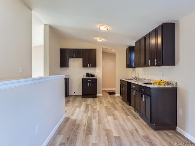 kitchen featuring light hardwood / wood-style floors, light stone counters, dark brown cabinetry, sink, and lofted ceiling