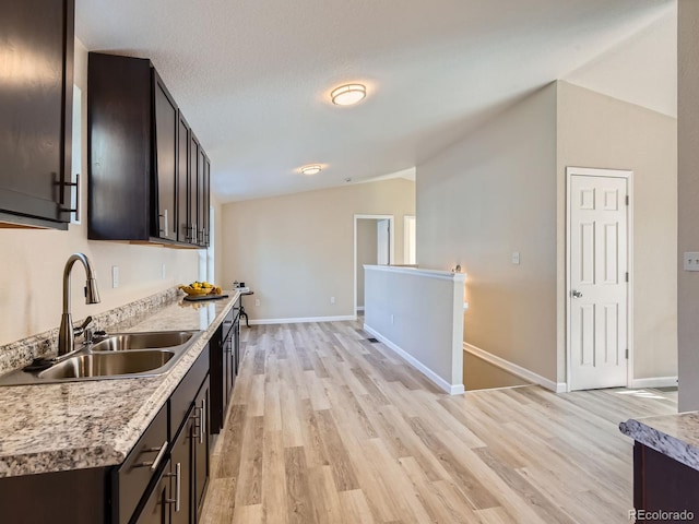 kitchen with light stone countertops, vaulted ceiling, light hardwood / wood-style flooring, sink, and dark brown cabinetry