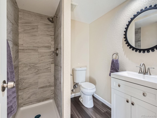 bathroom featuring a tile shower, toilet, vanity, and wood-type flooring