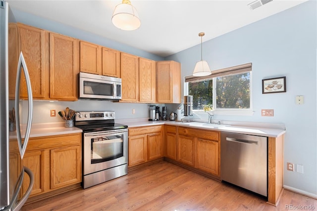 kitchen featuring decorative light fixtures, sink, appliances with stainless steel finishes, and light hardwood / wood-style flooring