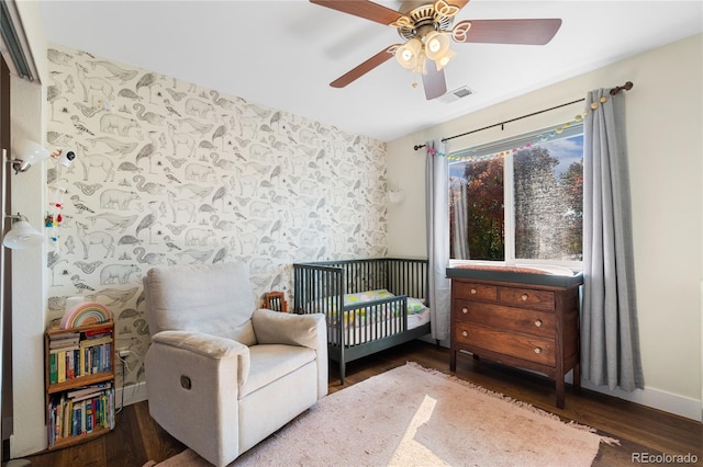 bedroom with ceiling fan, dark hardwood / wood-style flooring, and a crib