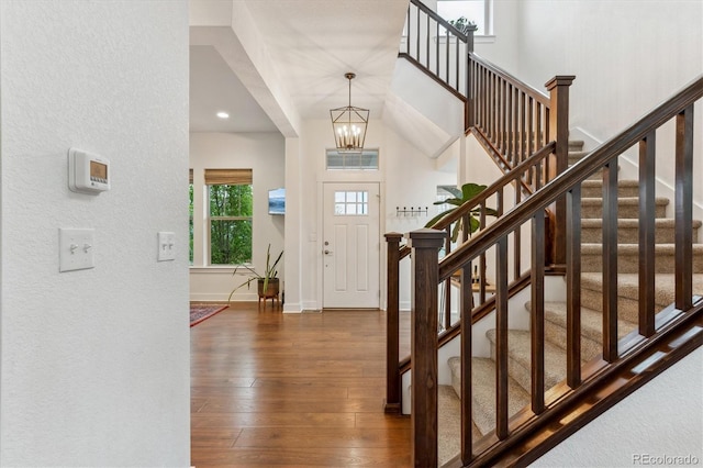 foyer entrance featuring dark wood-style flooring, stairway, a chandelier, baseboards, and a textured wall