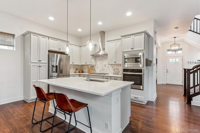 kitchen with appliances with stainless steel finishes, wall chimney exhaust hood, decorative backsplash, light countertops, and an island with sink