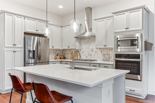 kitchen with appliances with stainless steel finishes, wall chimney exhaust hood, wood finished floors, a kitchen breakfast bar, and recessed lighting