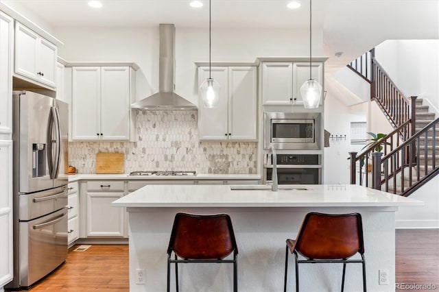 kitchen featuring appliances with stainless steel finishes, wall chimney range hood, a sink, light wood-type flooring, and backsplash