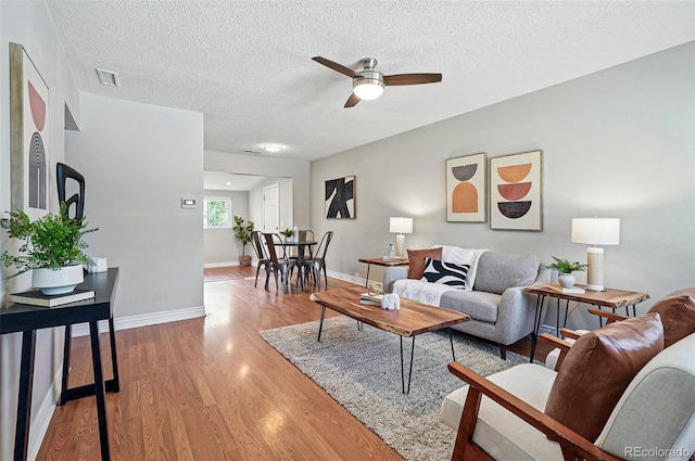living room featuring a ceiling fan, light wood-type flooring, a textured ceiling, and baseboards