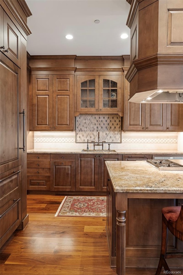 kitchen featuring light stone countertops, sink, stainless steel gas cooktop, light hardwood / wood-style flooring, and backsplash