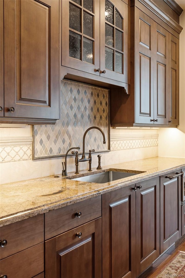 kitchen with decorative backsplash, wood-type flooring, light stone countertops, and sink