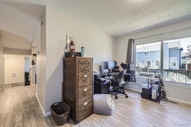 office space featuring a textured ceiling, vaulted ceiling, light wood-type flooring, and baseboards