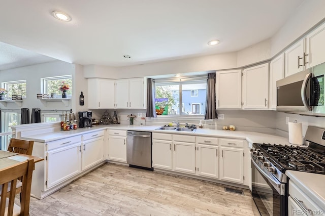 kitchen with stainless steel appliances, a peninsula, a sink, visible vents, and white cabinets