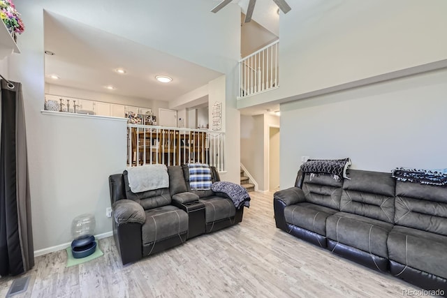 living room featuring light wood-style flooring, visible vents, baseboards, a ceiling fan, and stairway