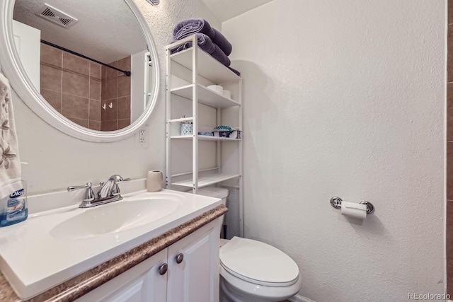 bathroom featuring visible vents, a textured wall, vanity, and toilet