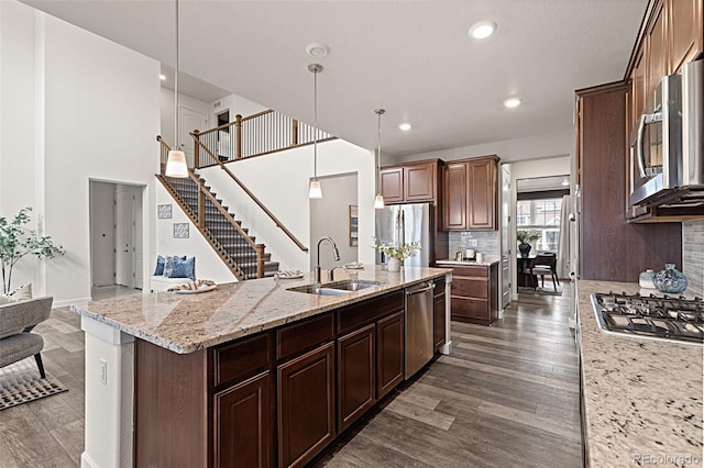 kitchen with a kitchen island with sink, pendant lighting, stainless steel appliances, a sink, and dark wood-style floors