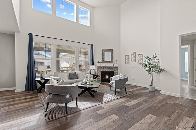 living area featuring baseboards, a tile fireplace, wood finished floors, and a towering ceiling