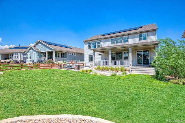 back of property with a patio area, fence, roof mounted solar panels, a lawn, and covered porch