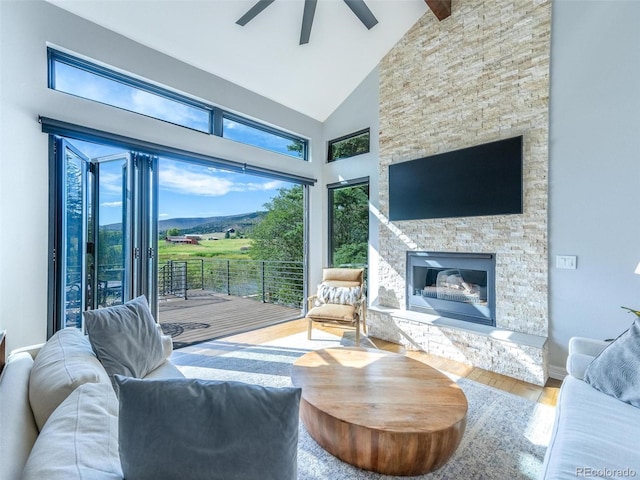 living room featuring ceiling fan, high vaulted ceiling, a stone fireplace, and hardwood / wood-style floors