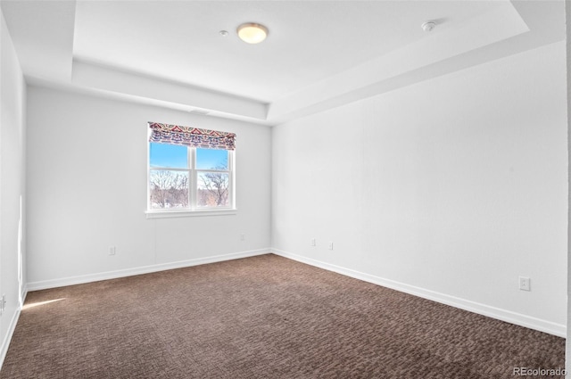 spare room with a raised ceiling and dark carpet