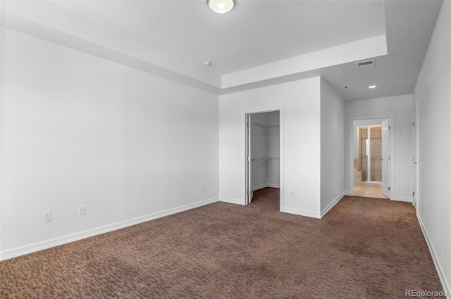 unfurnished bedroom with dark carpet, a walk in closet, and a closet