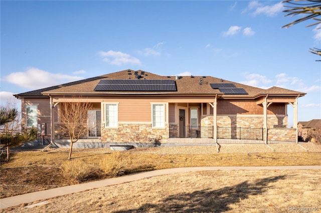 rear view of property with stone siding, covered porch, solar panels, and roof with shingles