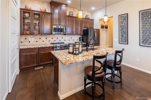 kitchen featuring appliances with stainless steel finishes, dark wood-style flooring, light stone counters, and decorative backsplash