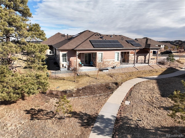 view of front of property with stone siding, a shingled roof, a patio area, and roof mounted solar panels