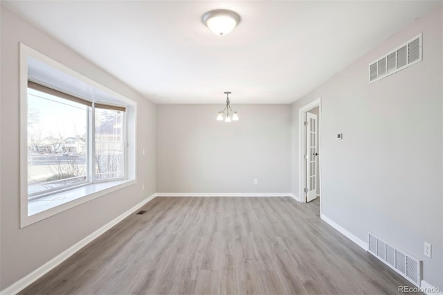 unfurnished room with wood finished floors, a notable chandelier, baseboards, and visible vents