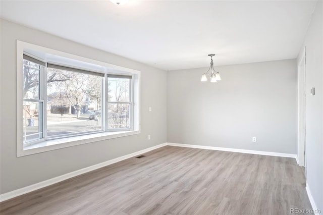 spare room featuring a notable chandelier, visible vents, baseboards, and wood finished floors