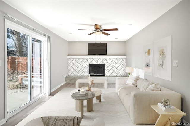 living room with baseboards, a ceiling fan, wood finished floors, and a tiled fireplace