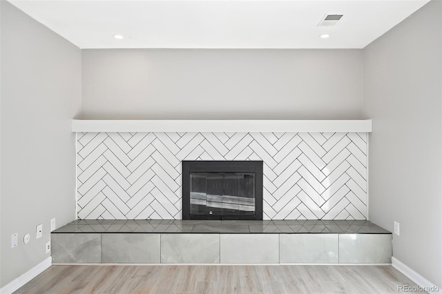 details featuring visible vents, wood finished floors, baseboards, and a glass covered fireplace