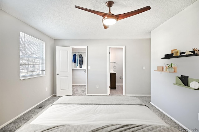 bedroom with a spacious closet, connected bathroom, baseboards, carpet flooring, and a textured ceiling