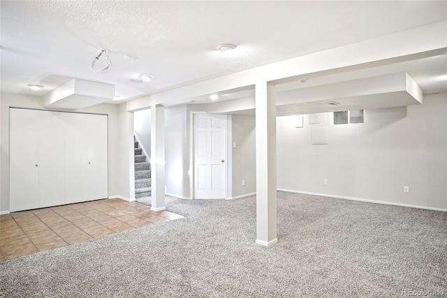 finished below grade area with stairway, baseboards, a textured ceiling, tile patterned floors, and carpet flooring