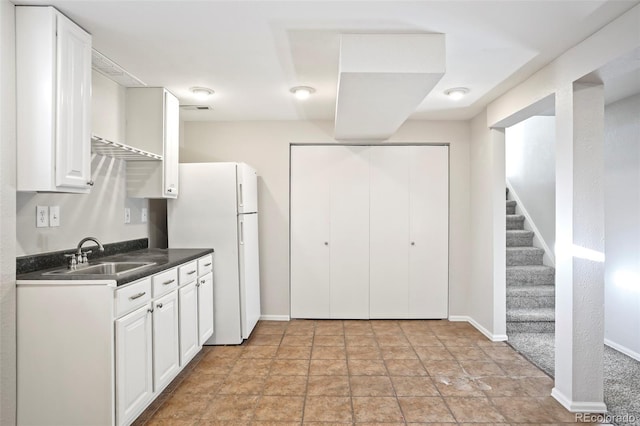 kitchen featuring a sink, dark countertops, freestanding refrigerator, white cabinets, and baseboards