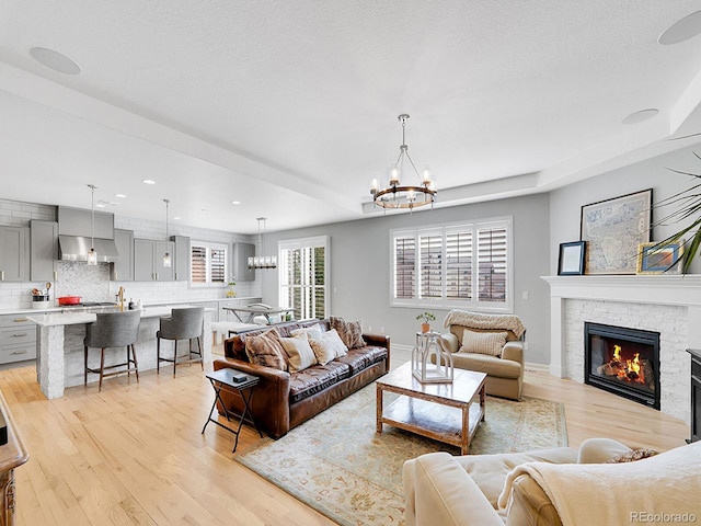 living room with baseboards, a chandelier, recessed lighting, a fireplace, and light wood-style floors