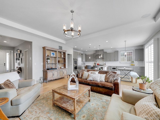 living area featuring a notable chandelier, recessed lighting, light wood-type flooring, and a tray ceiling