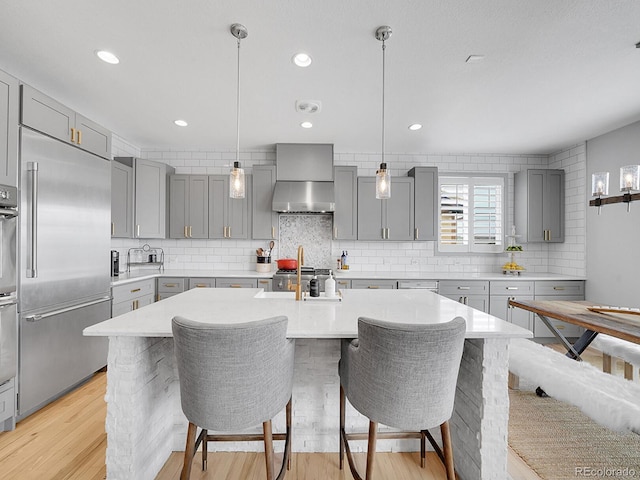 kitchen featuring gray cabinetry, light countertops, built in fridge, light wood-type flooring, and backsplash