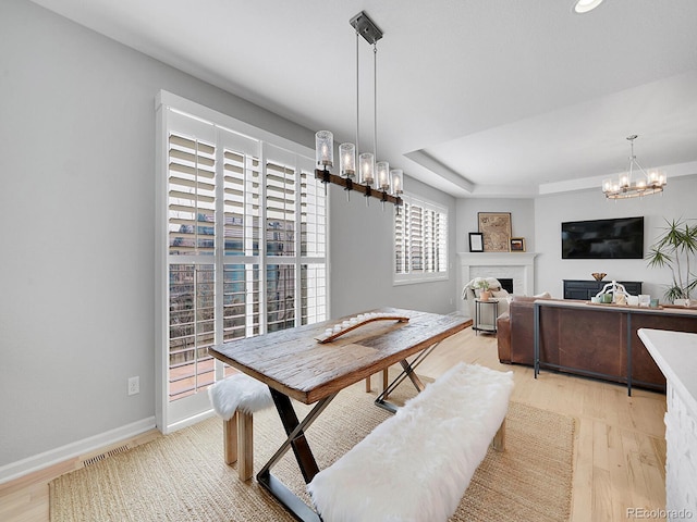 dining room featuring baseboards, an inviting chandelier, a tray ceiling, a fireplace, and light wood-type flooring