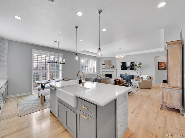 kitchen with a fireplace, a sink, gray cabinetry, dishwasher, and a chandelier