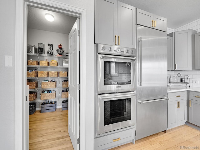 kitchen featuring gray cabinetry, light wood-type flooring, decorative backsplash, a textured ceiling, and stainless steel appliances