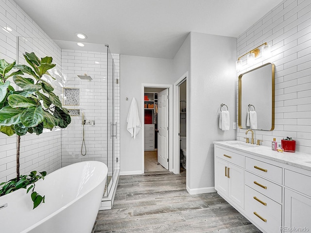 bathroom with vanity, wood finished floors, a soaking tub, a shower stall, and a walk in closet