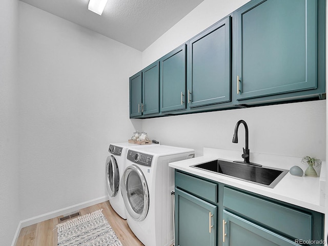 laundry room with visible vents, a sink, washing machine and dryer, cabinet space, and light wood finished floors