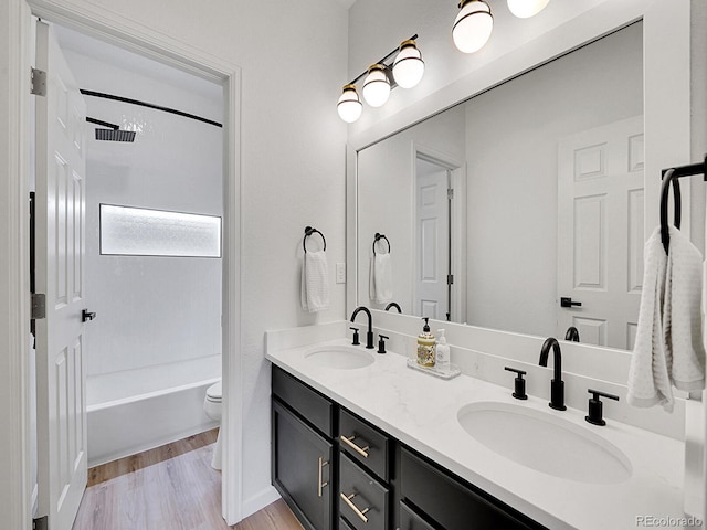 full bath with double vanity, toilet, wood finished floors, and a sink