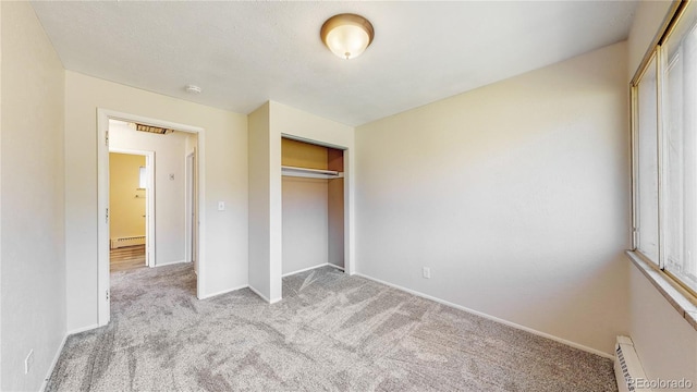 unfurnished bedroom with light colored carpet, a closet, and a baseboard heating unit