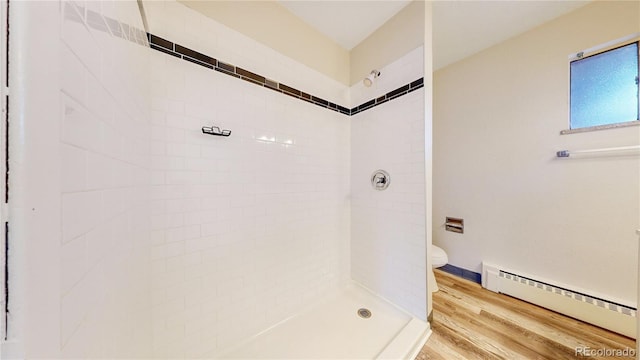 bathroom with a tile shower, toilet, a baseboard radiator, and hardwood / wood-style flooring