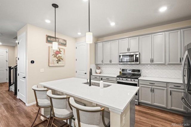 kitchen featuring a center island with sink, stainless steel appliances, pendant lighting, sink, and backsplash