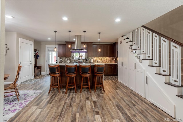 kitchen featuring dark wood-style floors, island exhaust hood, light countertops, backsplash, and a kitchen breakfast bar